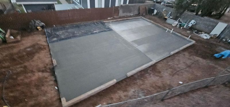 Backyard concrete slab being poured, with wooden forms and a partially finished gray surface