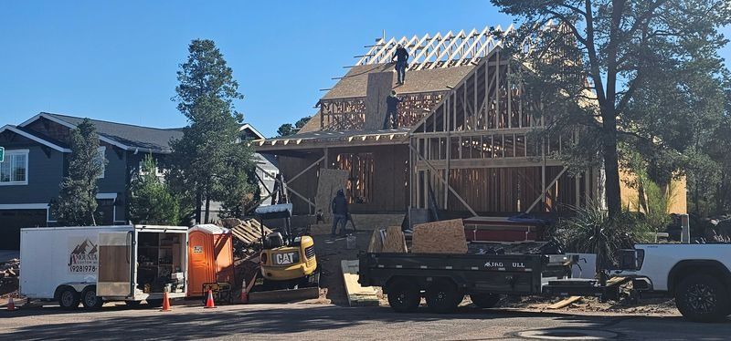House under construction with exposed roof framing, work trucks, and equipment in front of it