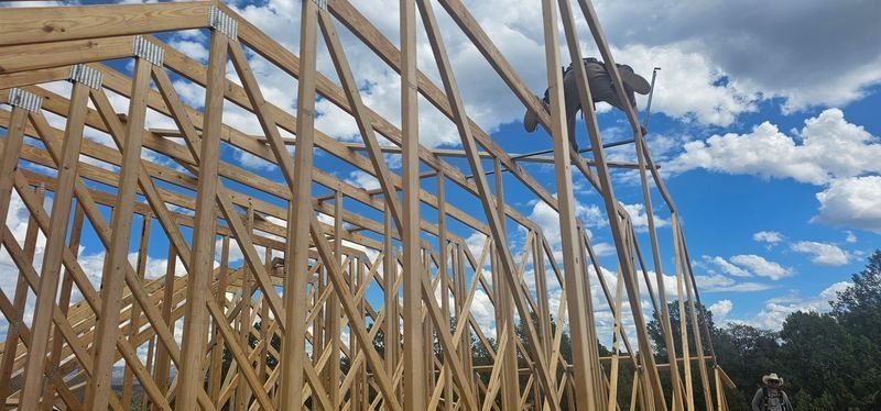 Wooden roof trusses under construction against a blue sky with clouds