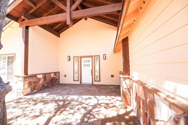 Covered porch with wood beams, white siding, stone base, and double glass doors in bright sunlight