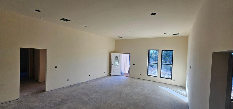 Empty unfurnished room with beige walls, gray floor, and large windows and doorway letting in daylight