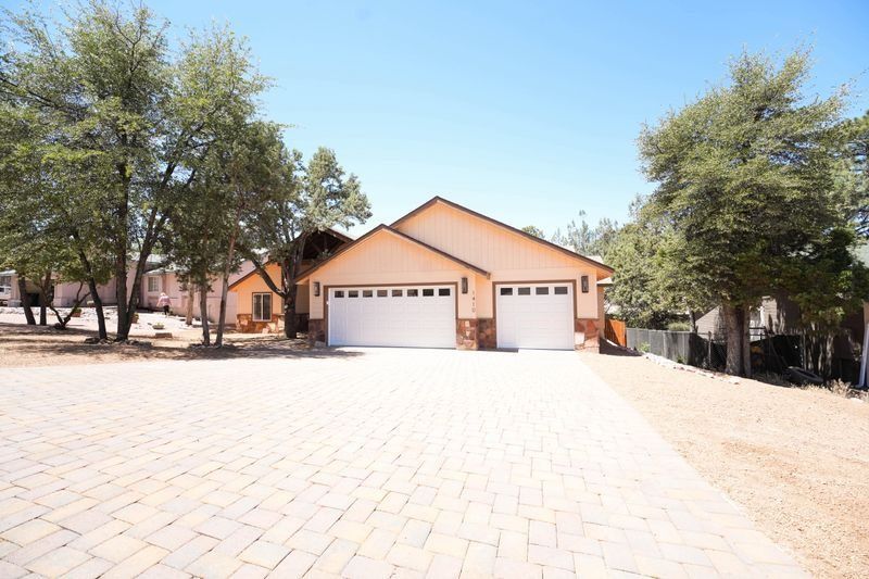 Single-story beige house with a double garage, large paved driveway, and trees on both sides