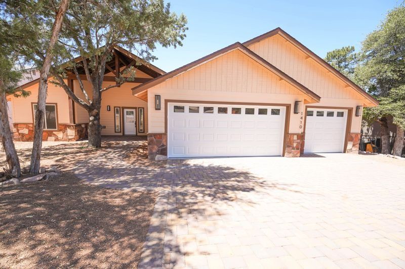 Suburban house with beige stucco exterior, two-car garage, and large tree in front yard