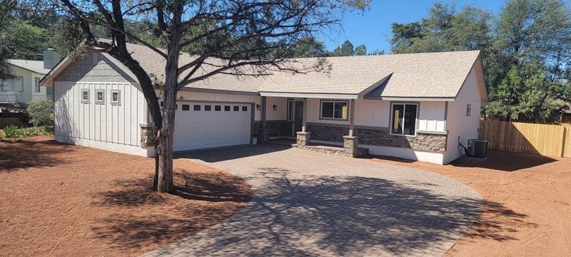 Single-story beige house with garage, front porch, and desert landscaping under a clear sky