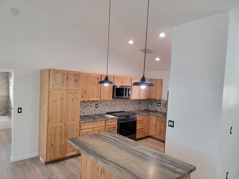 Modern kitchen with wood cabinets, patterned backsplash, black appliances, and a striped island countertop