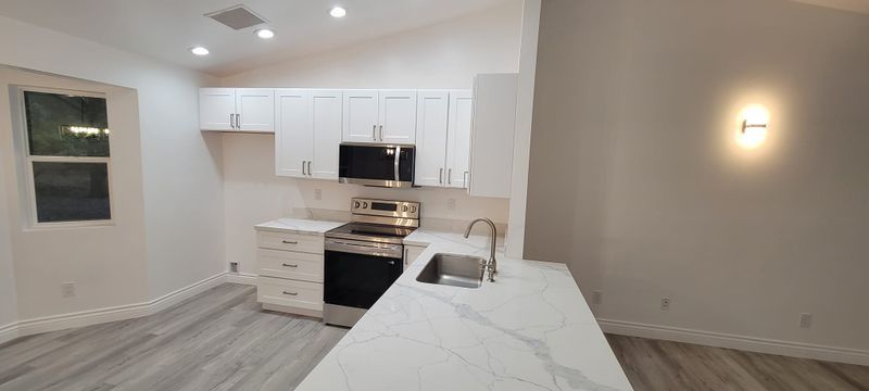 Modern white kitchen with island, stainless stove, wood floors, and wall sconces in an open room