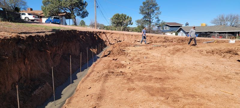 Workers on a dirt construction site with a deep trench and excavator nearby