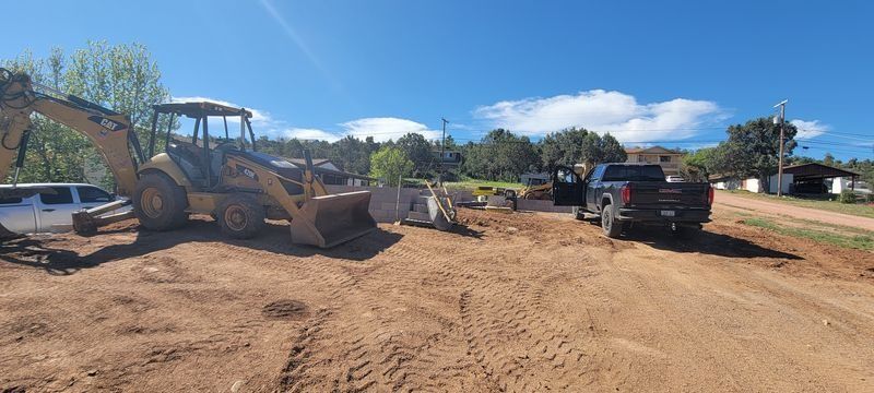 Construction site with a backhoe, pickup truck, and equipment on a dirt lot under a blue sky