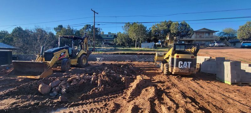 Two yellow construction machines on a muddy dirt lot under a clear blue sky