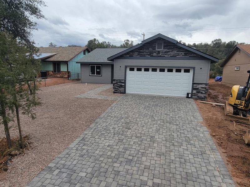 Front view of a gray house with a white garage and stone paver driveway.