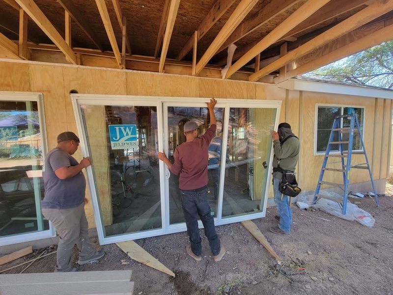 Three workers install large sliding glass doors on a patio under a wooden roof.