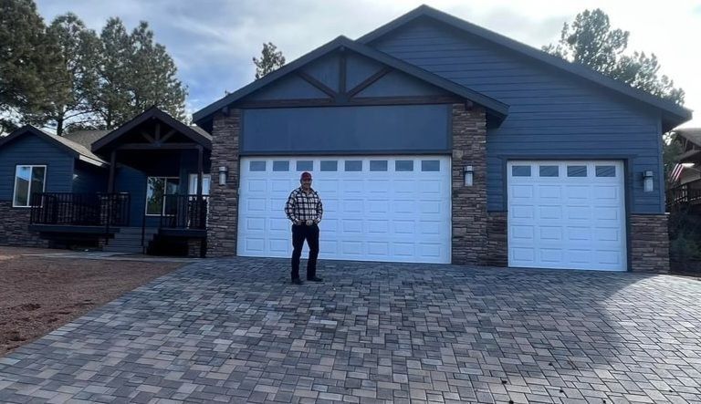 Person standing in front of a blue-gray house with a white garage door and paved driveway