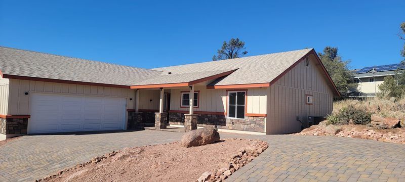 Single-story beige house with two-car garage, desert landscaping, and blue sky