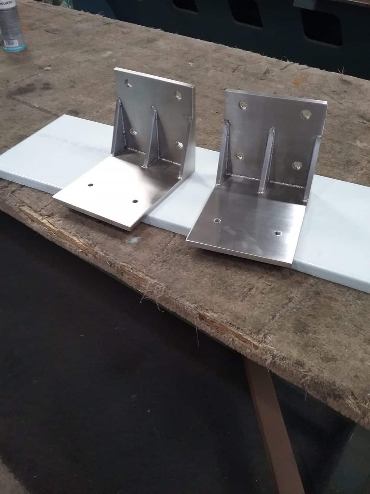 Two Shiny, Metal L-shaped Brackets Sit on a White Surface — Highlander Metals in Kirrawee, NSW
