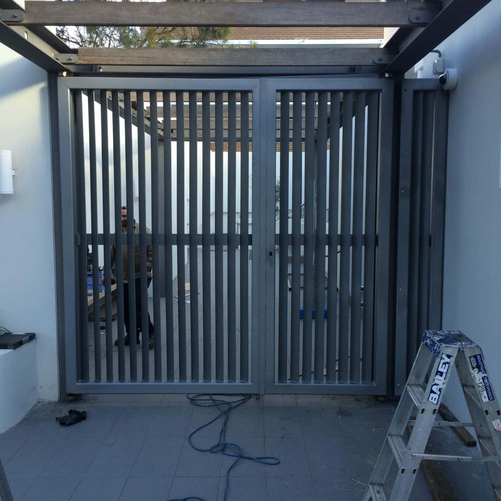 Gray Metal Gate With Vertical Slats. Man Stands Behind It — Highlander Metals in Kirrawee, NSW