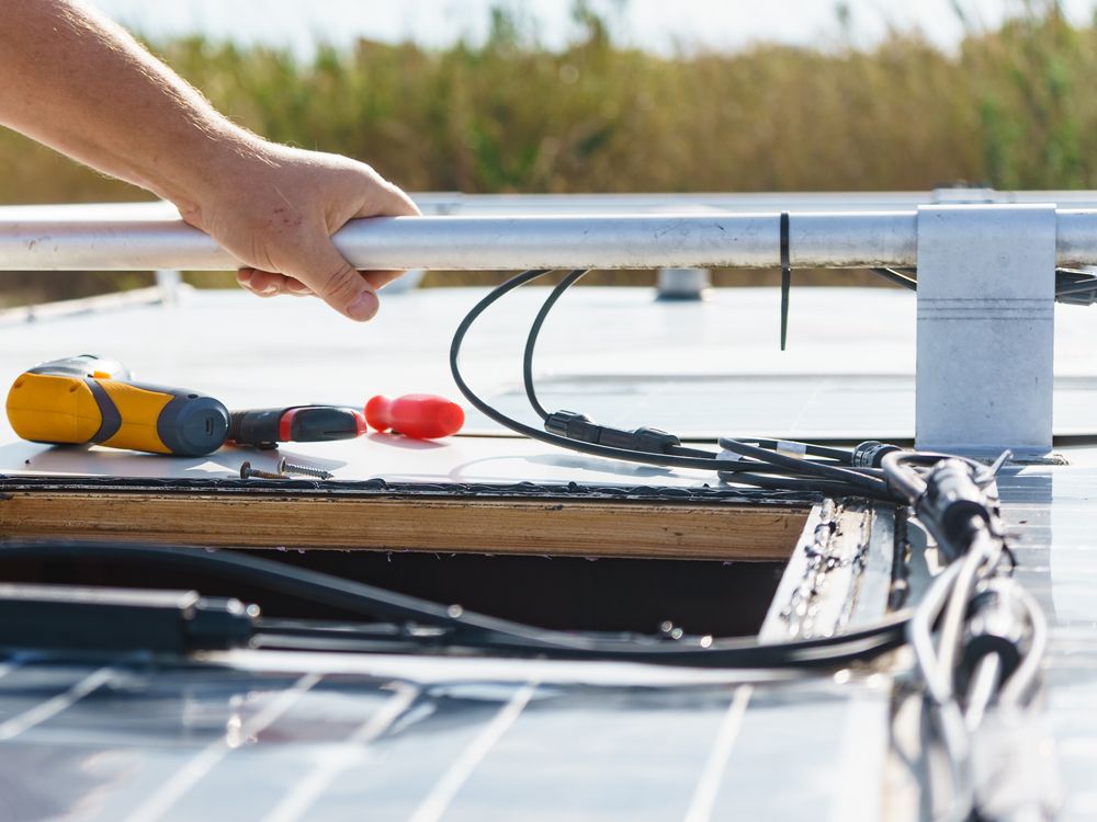 Hands working on rooftop solar panel wiring with tools and black cables