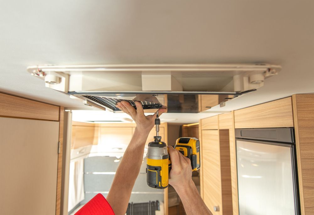 Hands using pliers to work on exposed electrical wiring inside a wall opening