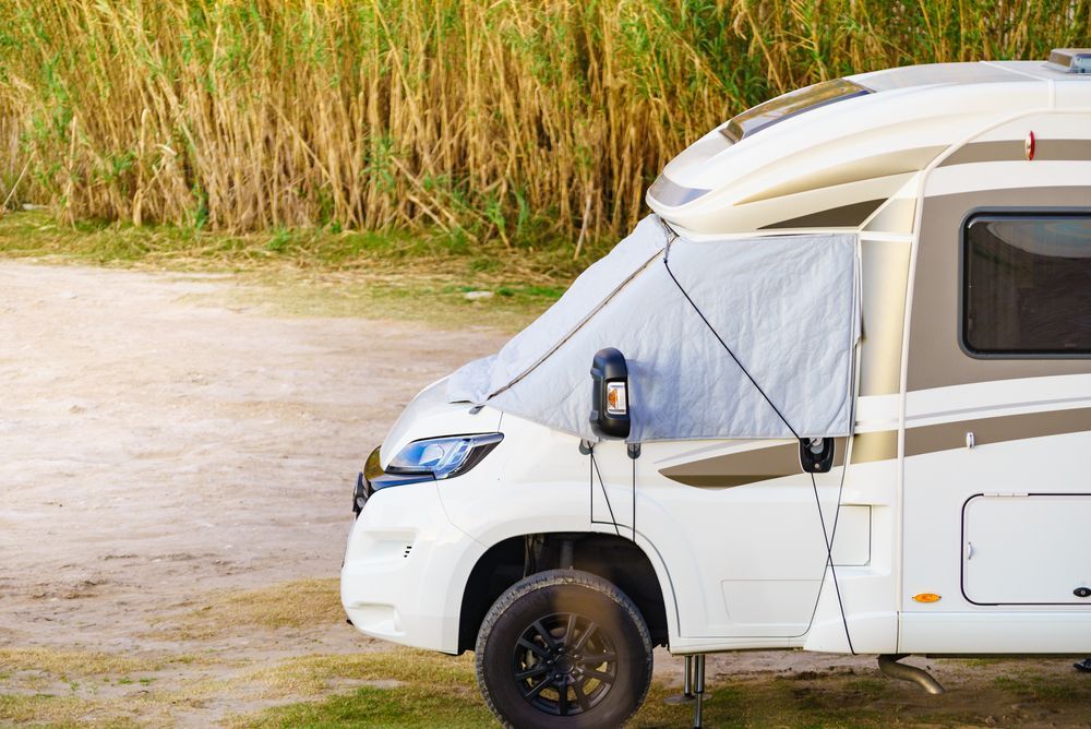 White camper van with a light gray sunshade extended, parked outdoors.