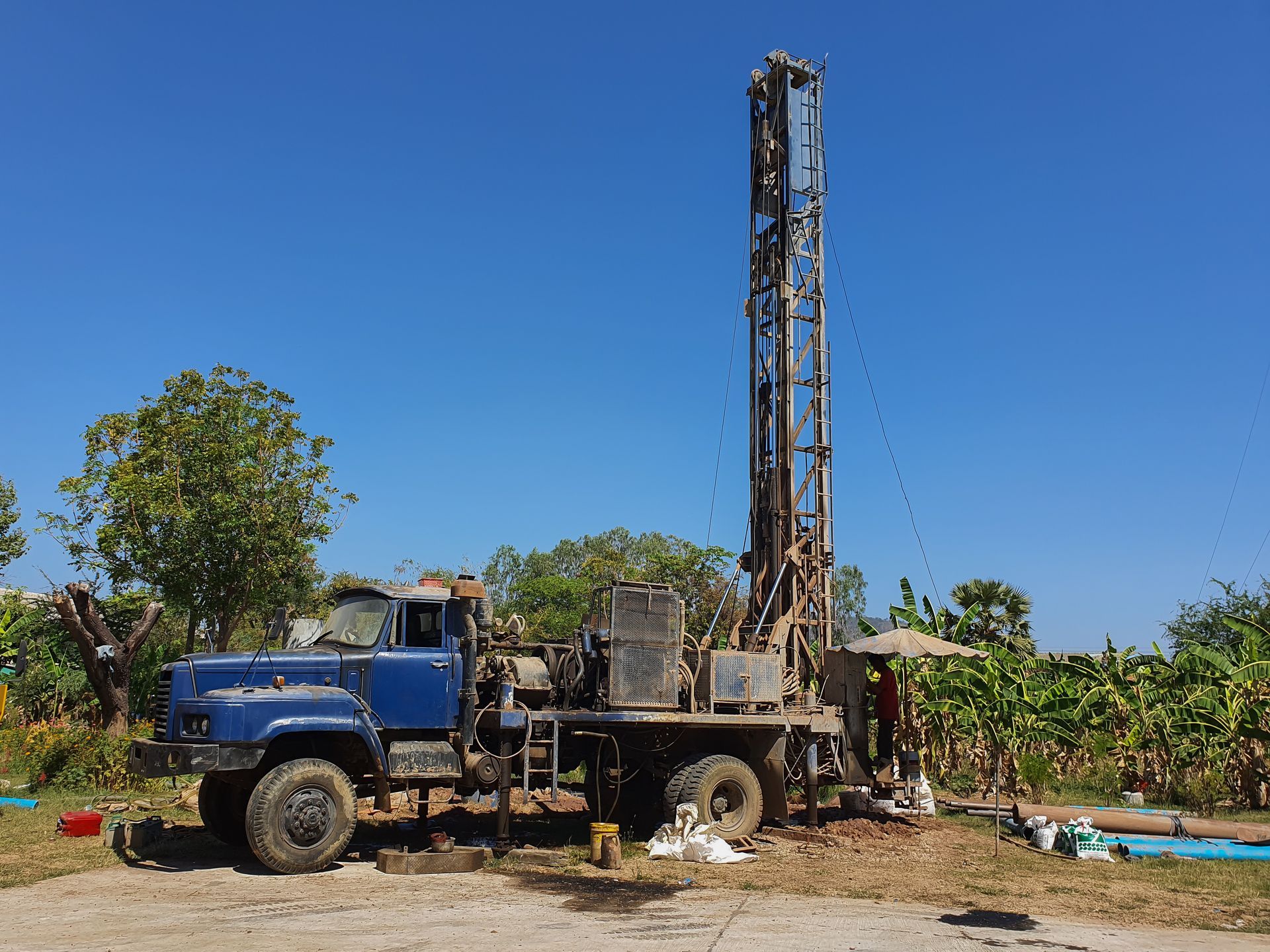 Blue drilling rig in field, under a bright blue sky.