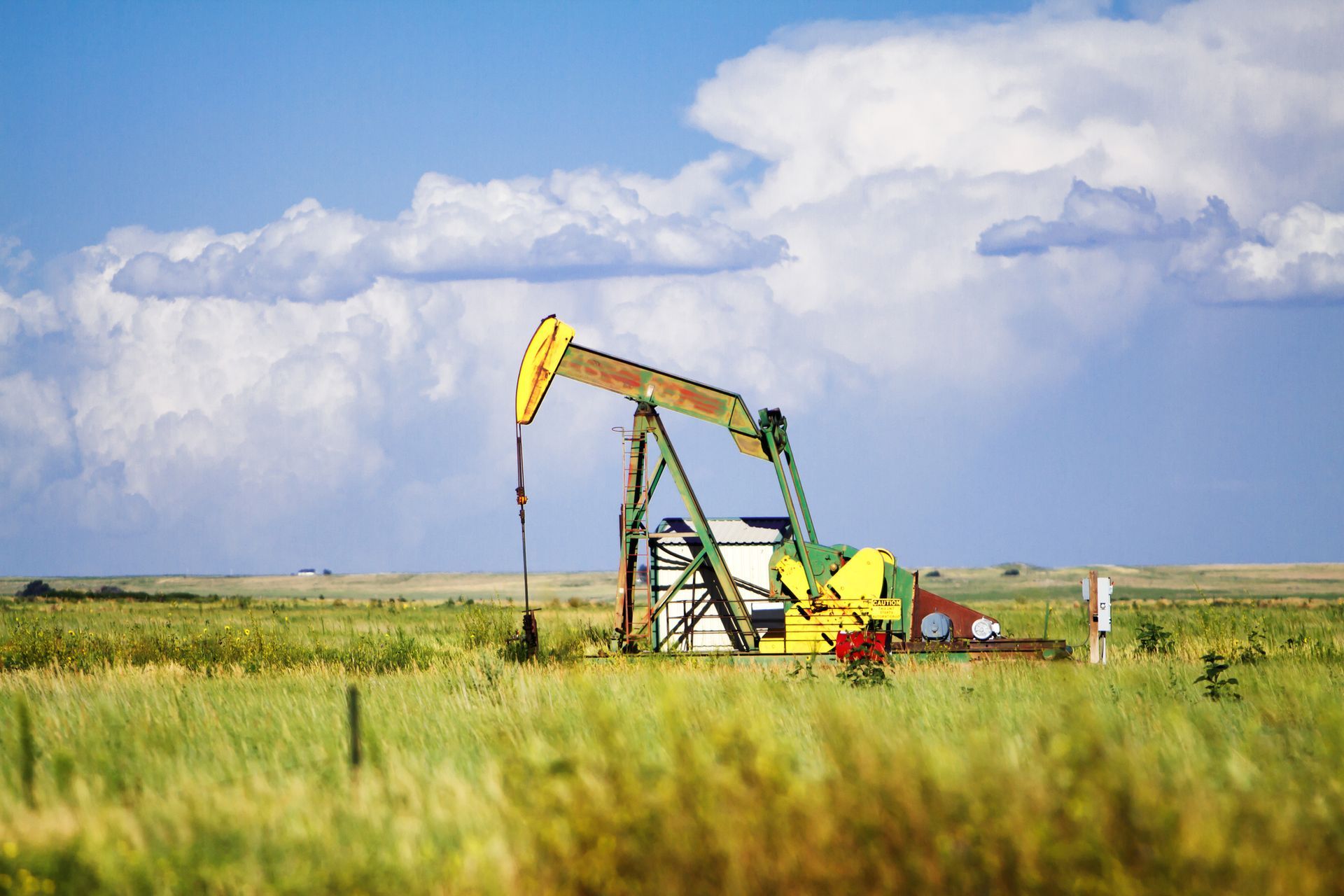 Oil pump jack in a grassy field under a cloudy blue sky.