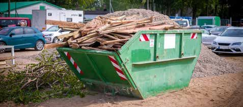 A green dumpster filled with wood is in a parking lot.