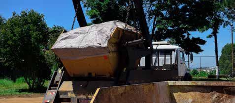 A dumpster is being lifted by a crane in a field.