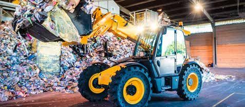 A yellow tractor is loading a pile of trash into a warehouse.