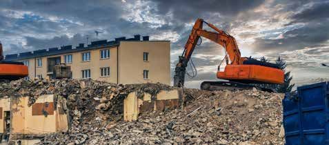 A large orange excavator is demolishing a building.