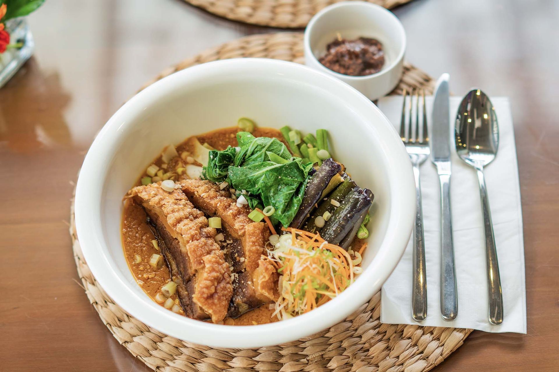 Filipino kare-kare bowl with crispy pork, eggplant, greens, and peanut sauc