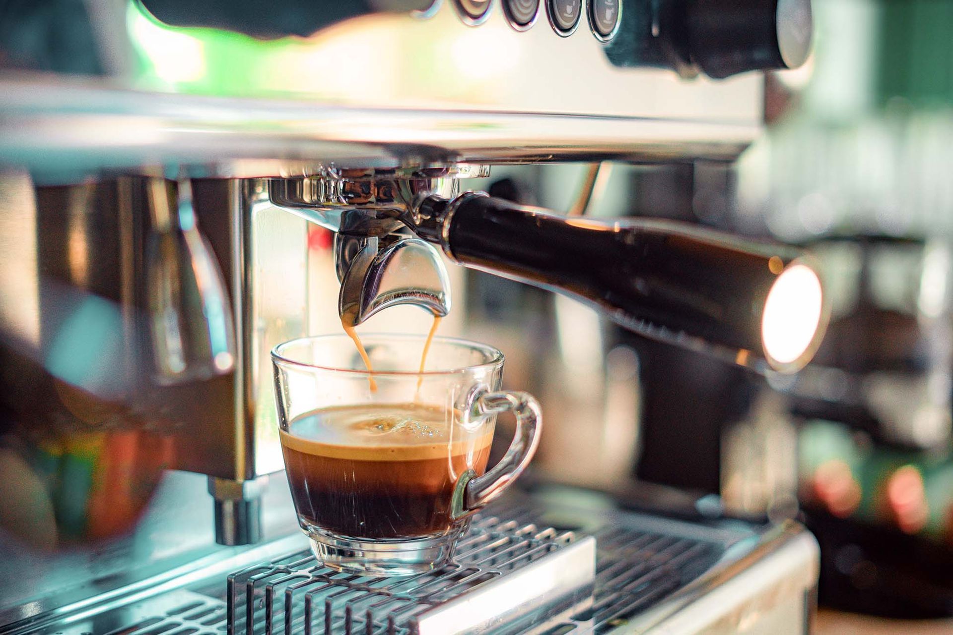 Espresso shot pouring into glass cup from chrome machine at Charlie's El Ni