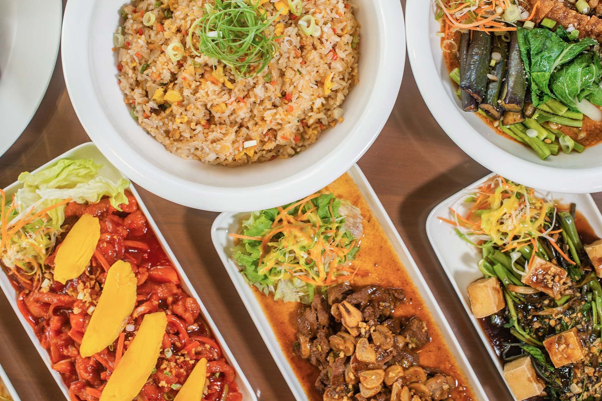 Assorted Asian dishes arranged on a table, including stir-fries, rice, and vegetables in white bowls.