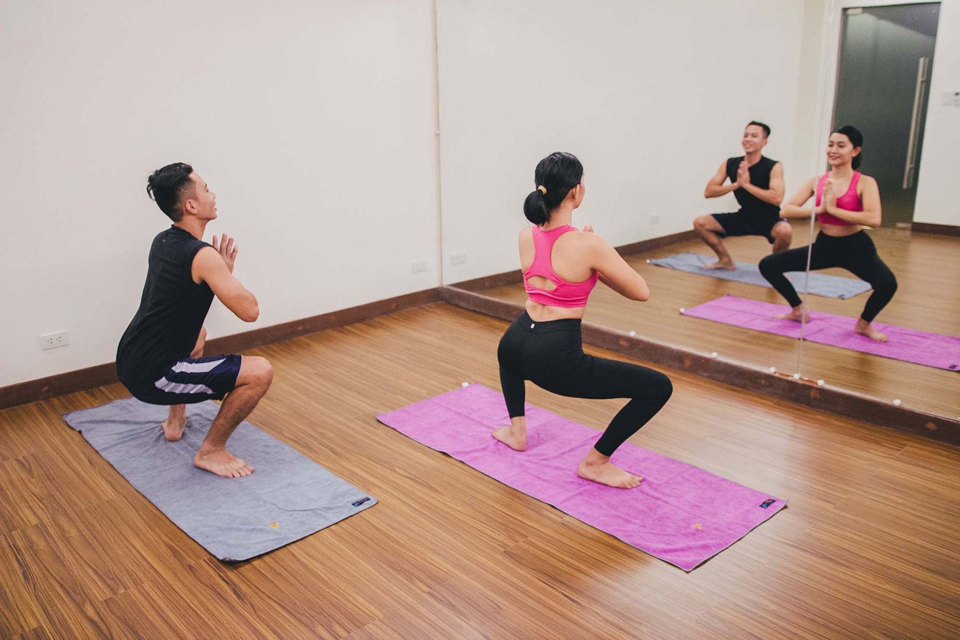 Two people doing squats on yoga mats in a mirrored studio