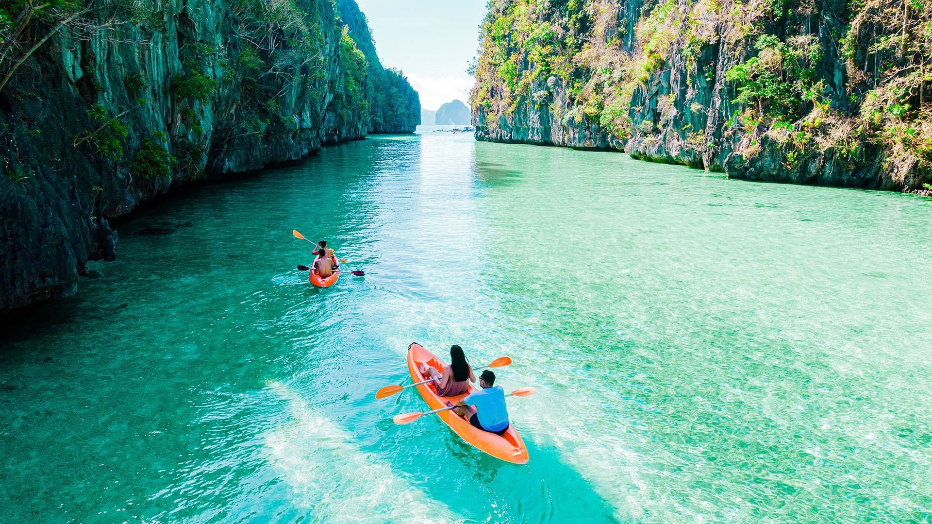 Kayakers on turquoise water between limestone cliffs.