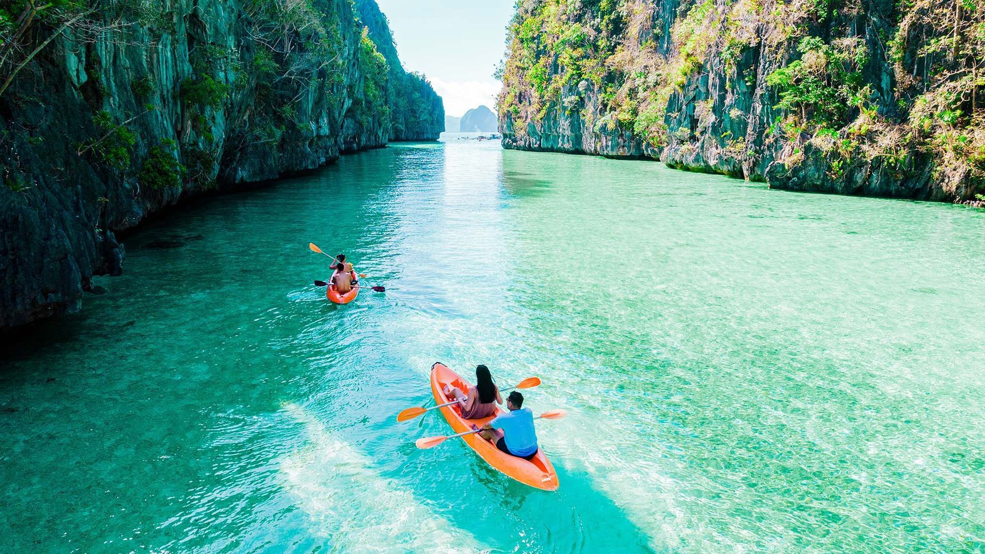 Two people kayaking in turquoise water between steep green cliffs