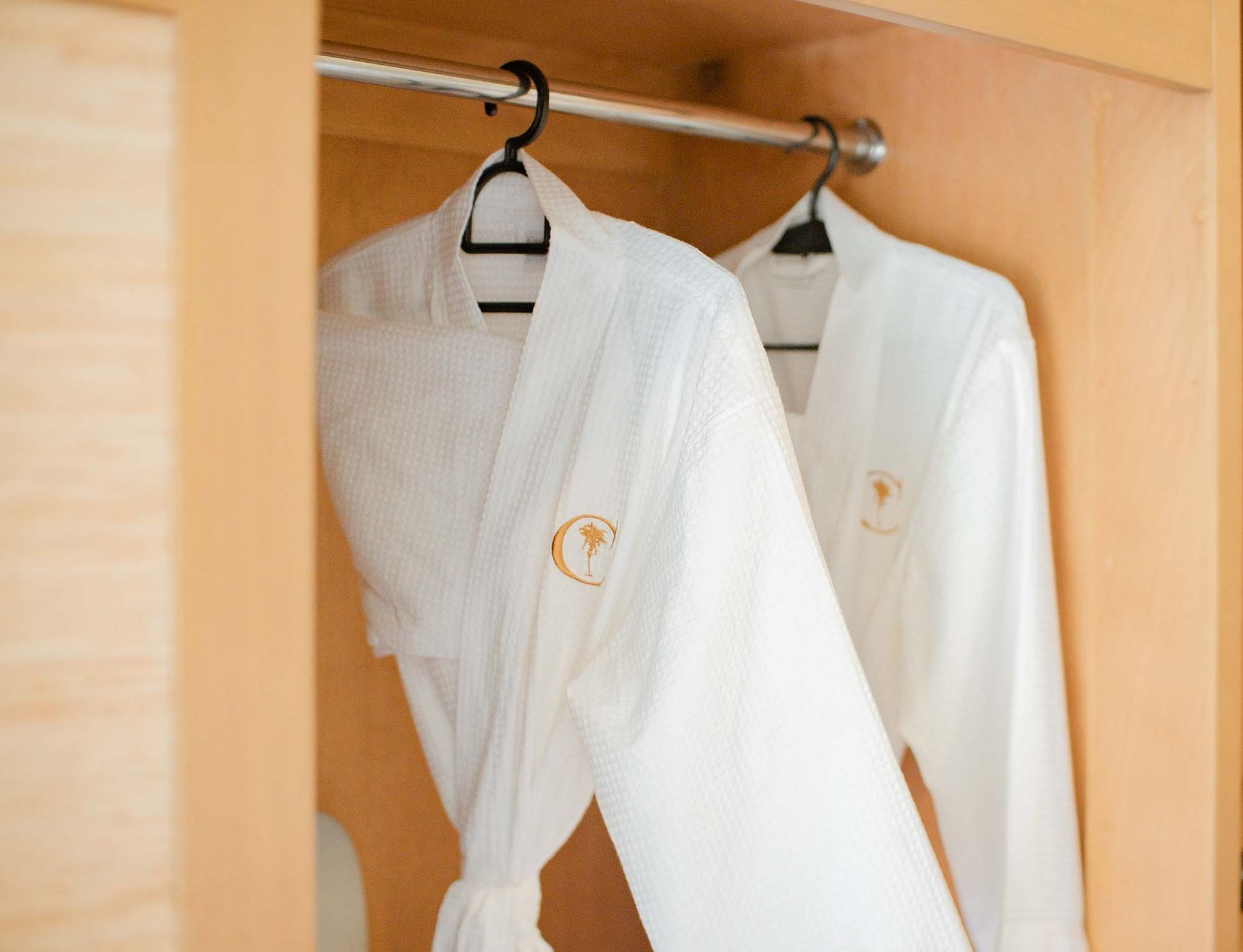 Two plush white bathrobes hanging in a wooden wardrobe