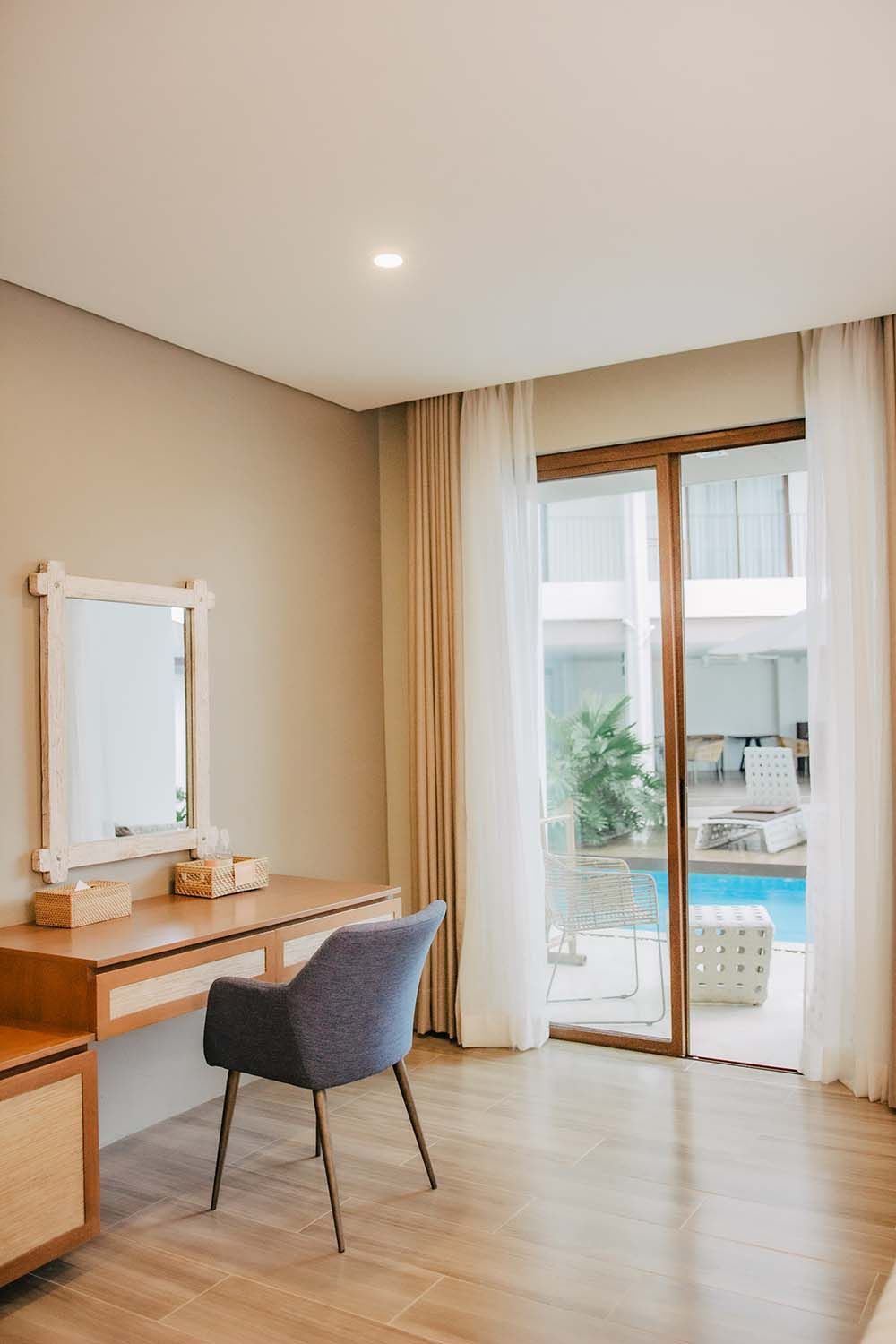Bright bedroom with a vanity desk, chair, and sliding doors opening to a poolside patio.