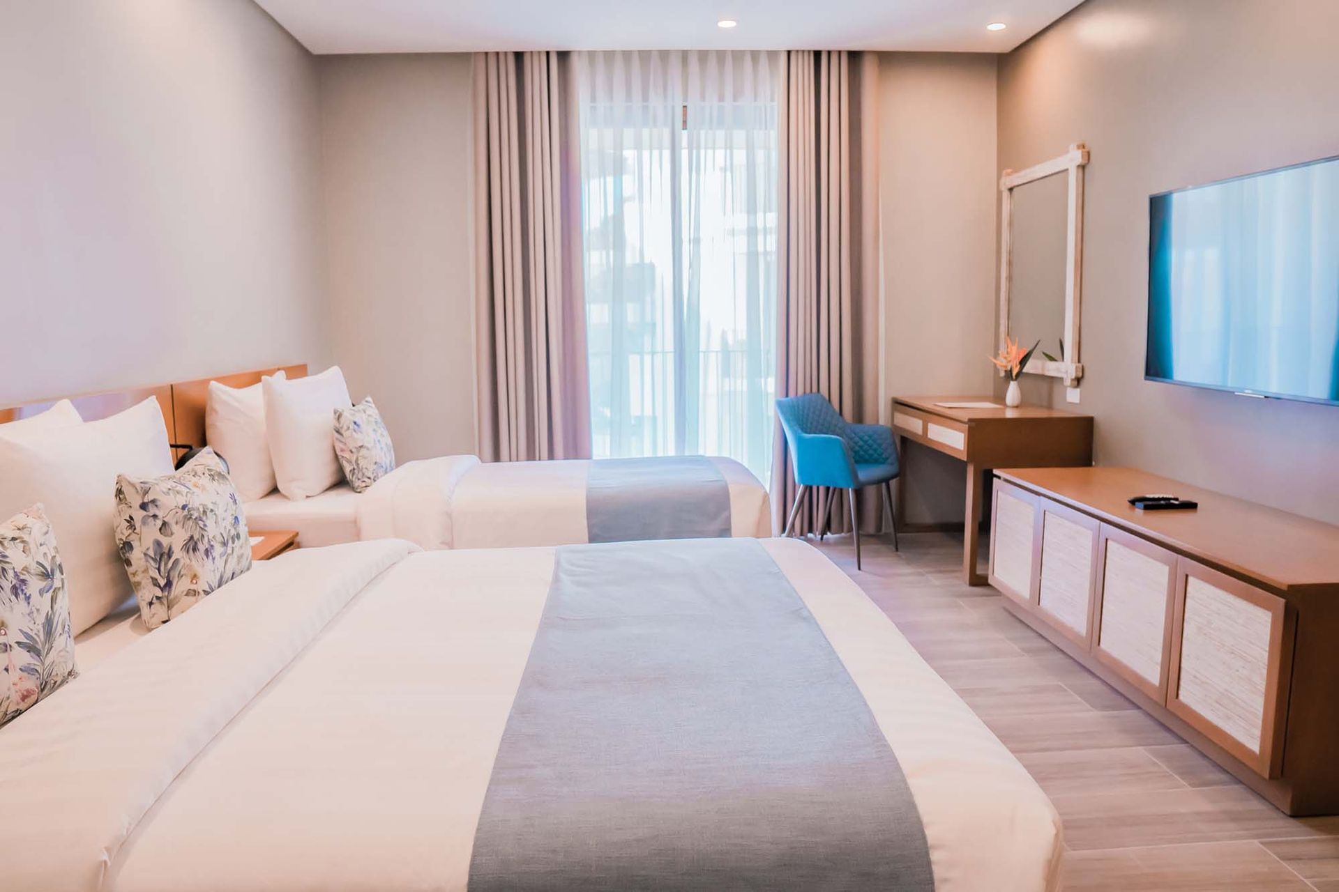 Family room with two comfortable beds, light blue runners, wooden furniture, vanity area and wall-mounted TV
