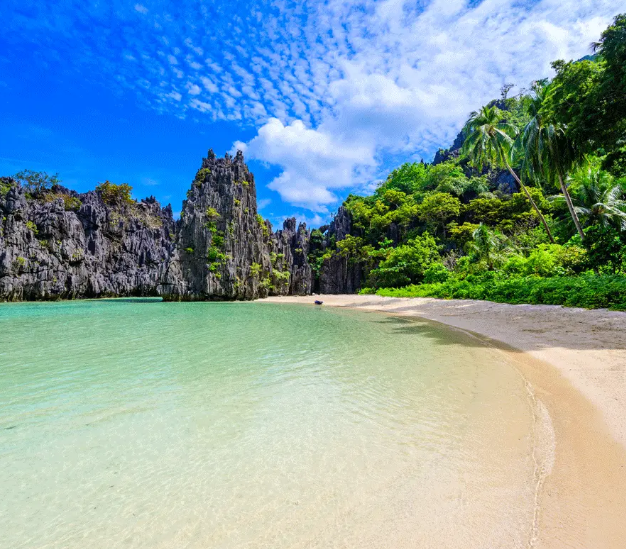 Tropical beach with turquoise water, white sand, and steep green limestone cliffs under a bright blue sky
