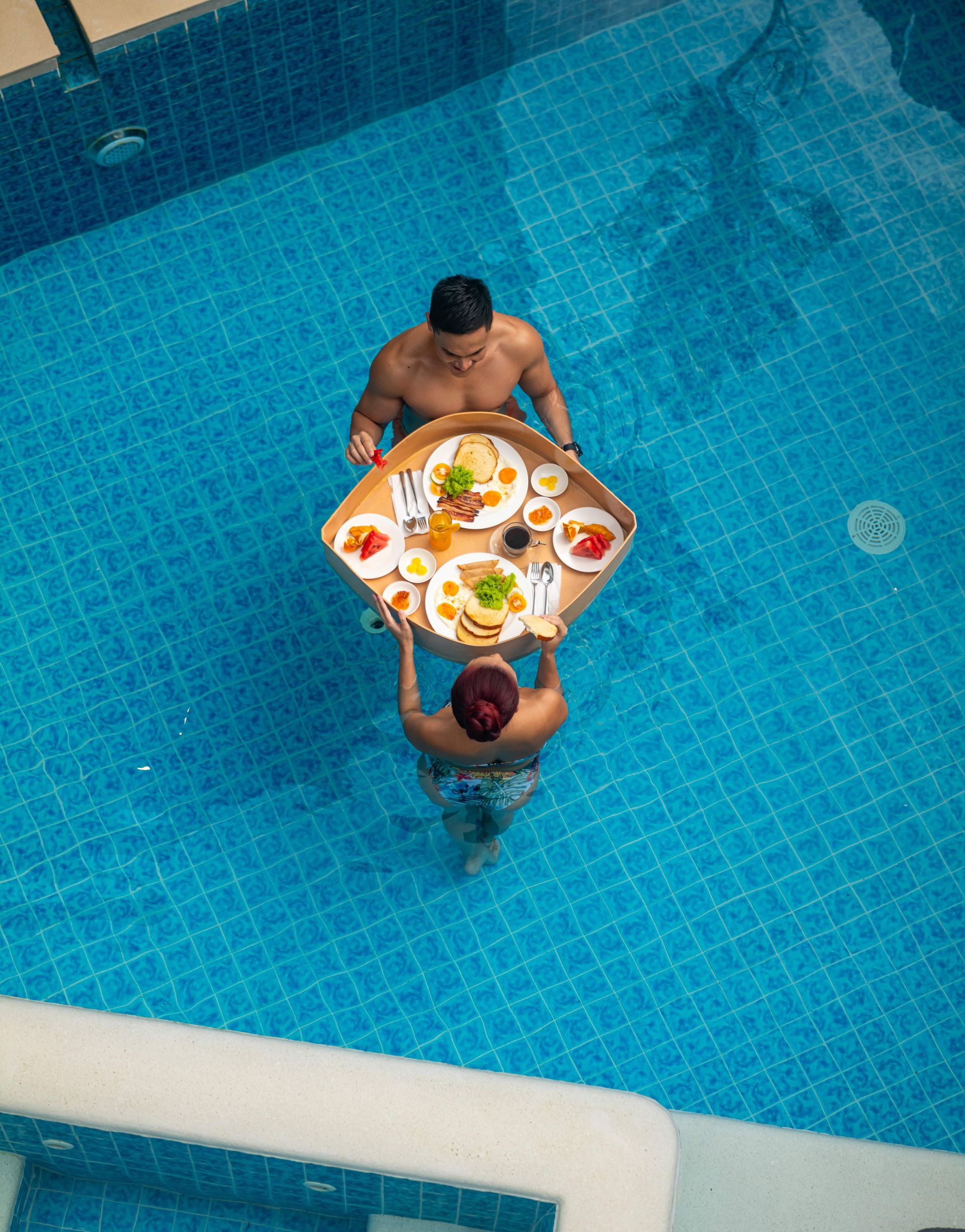 Two people in a blue pool passing a tray of food and drinks at Charlie's El Nido

