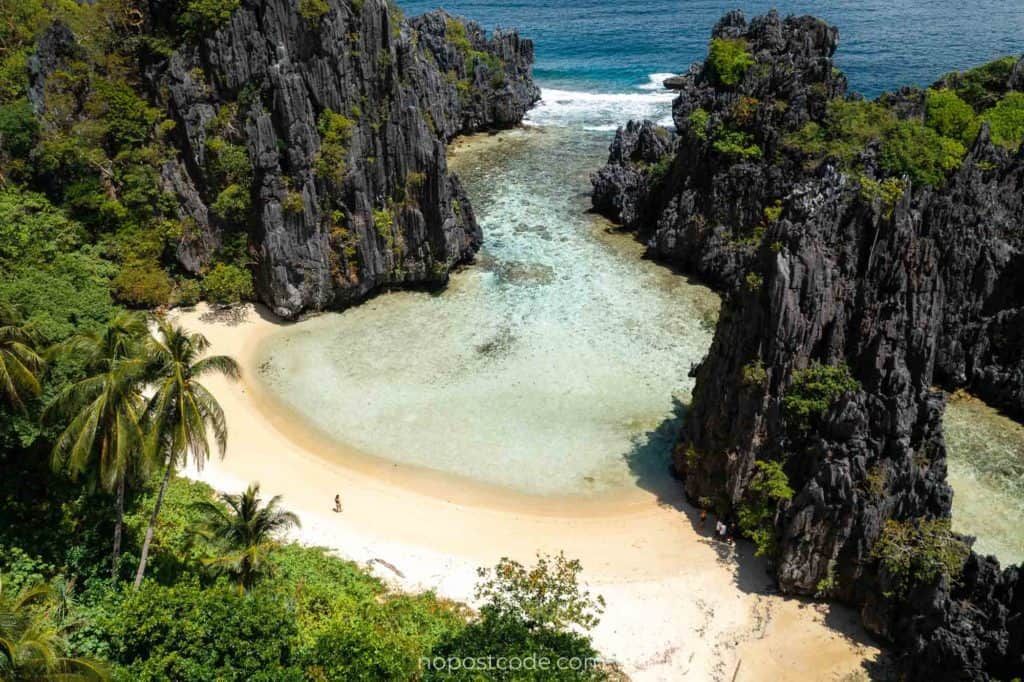Secluded tropical beach cove with clear turquoise water, white sand, and tall rocky cliffs