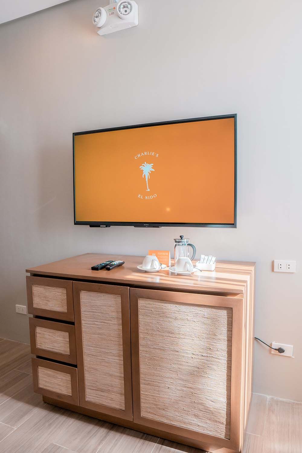 Wall-mounted flat-screen TV above a wooden desk with remote control and water carafe