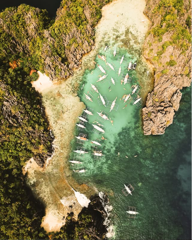 Aerial view of a turquoise cove with many white boats near rocky green cliffs