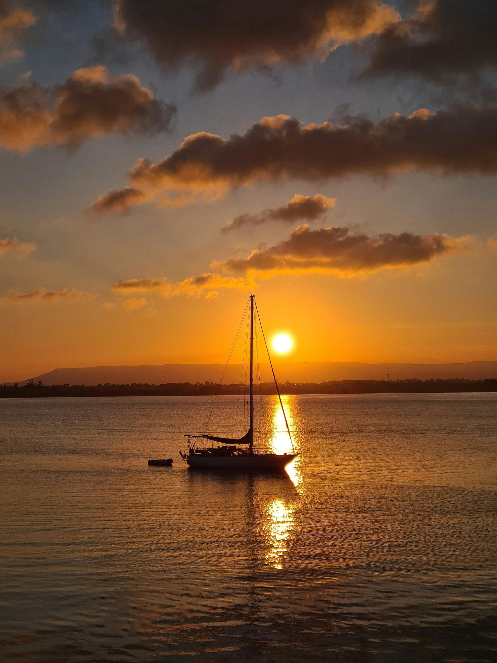 Sailboat at sunset on calm water, with golden sky and reflections.