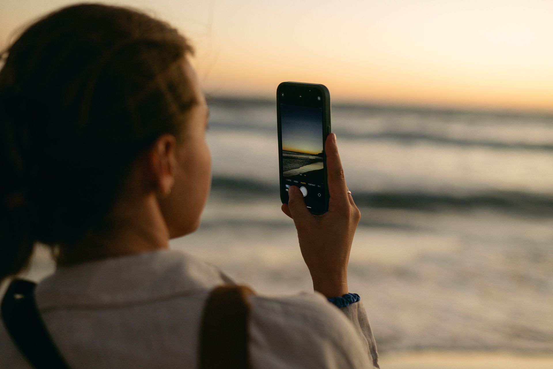 Person photographing a sunset over the ocean with a smartphone from the beach