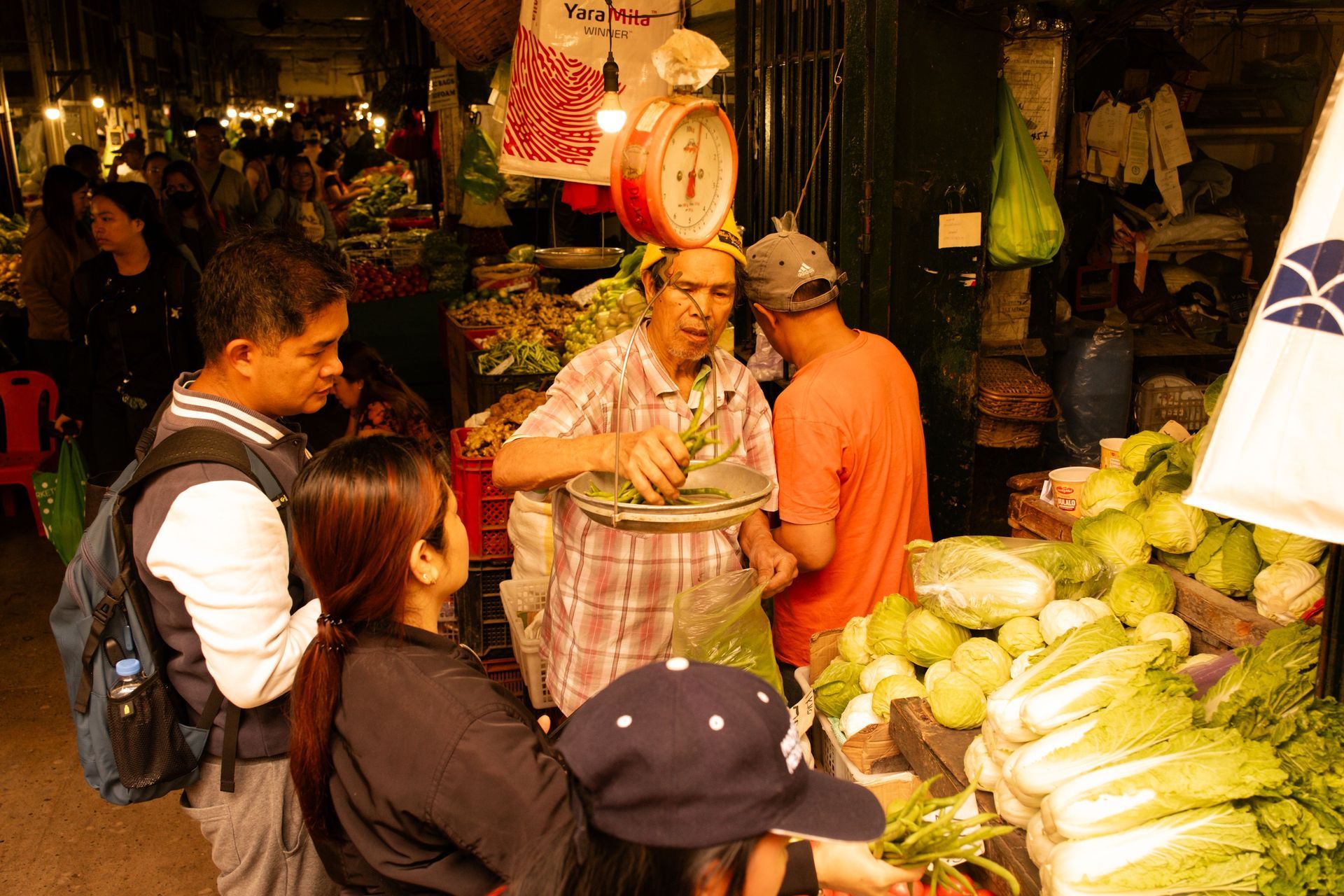 People shopping at a produce stall with corn and vegetables in a busy market