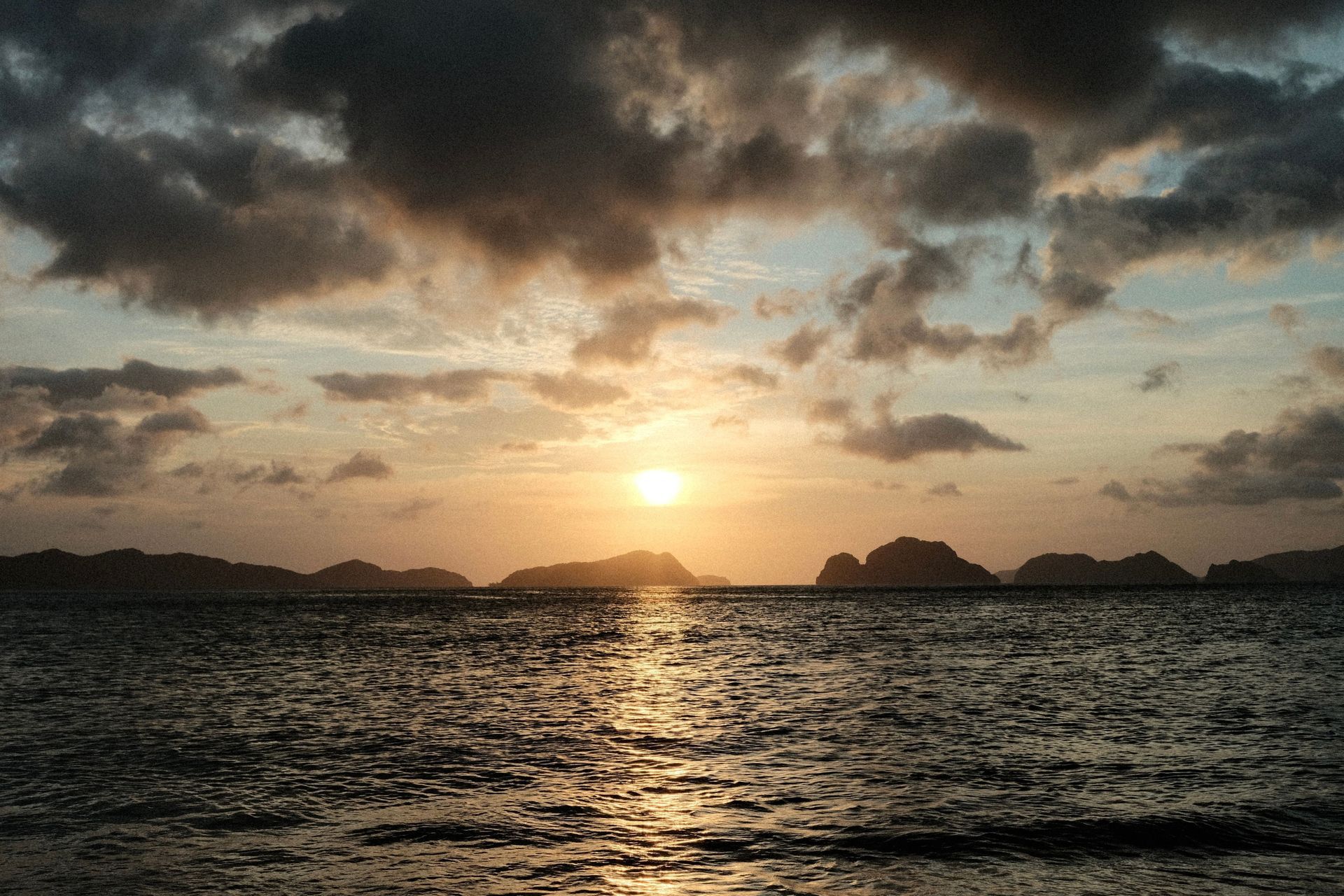 Sunset over a calm ocean with silhouetted islands and clouds reflecting on the water