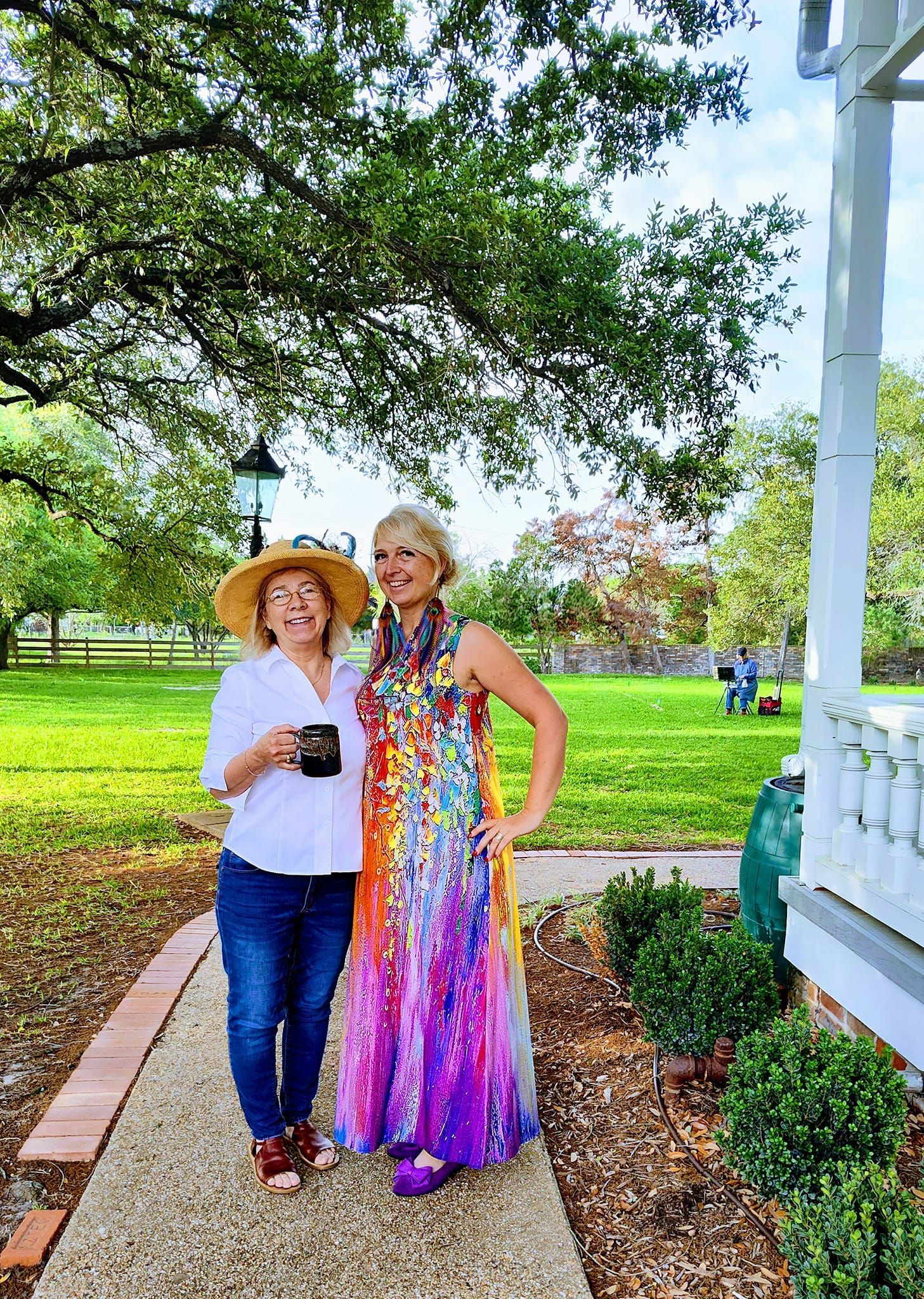 Two women are standing next to each other on a sidewalk in front of a house.