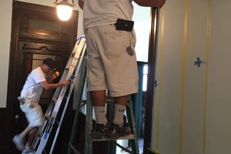 Two men are standing on a ladder painting a door