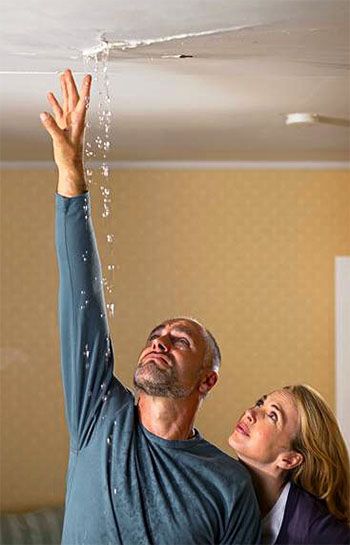 Man reaching for a leaking ceiling while a woman looks up at the water damage
