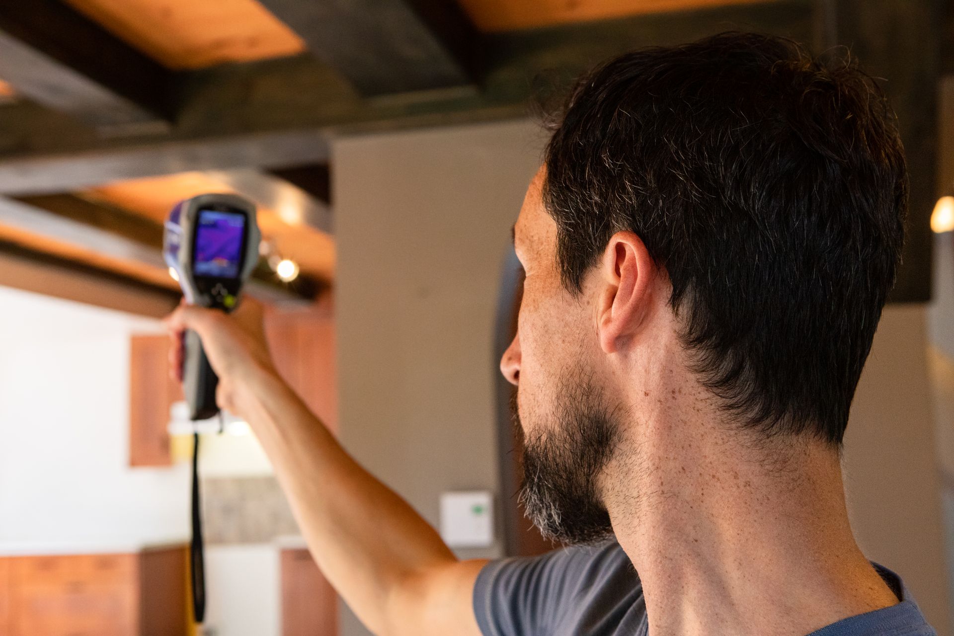 Person using a thermal camera to inspect a ceiling beam indoors